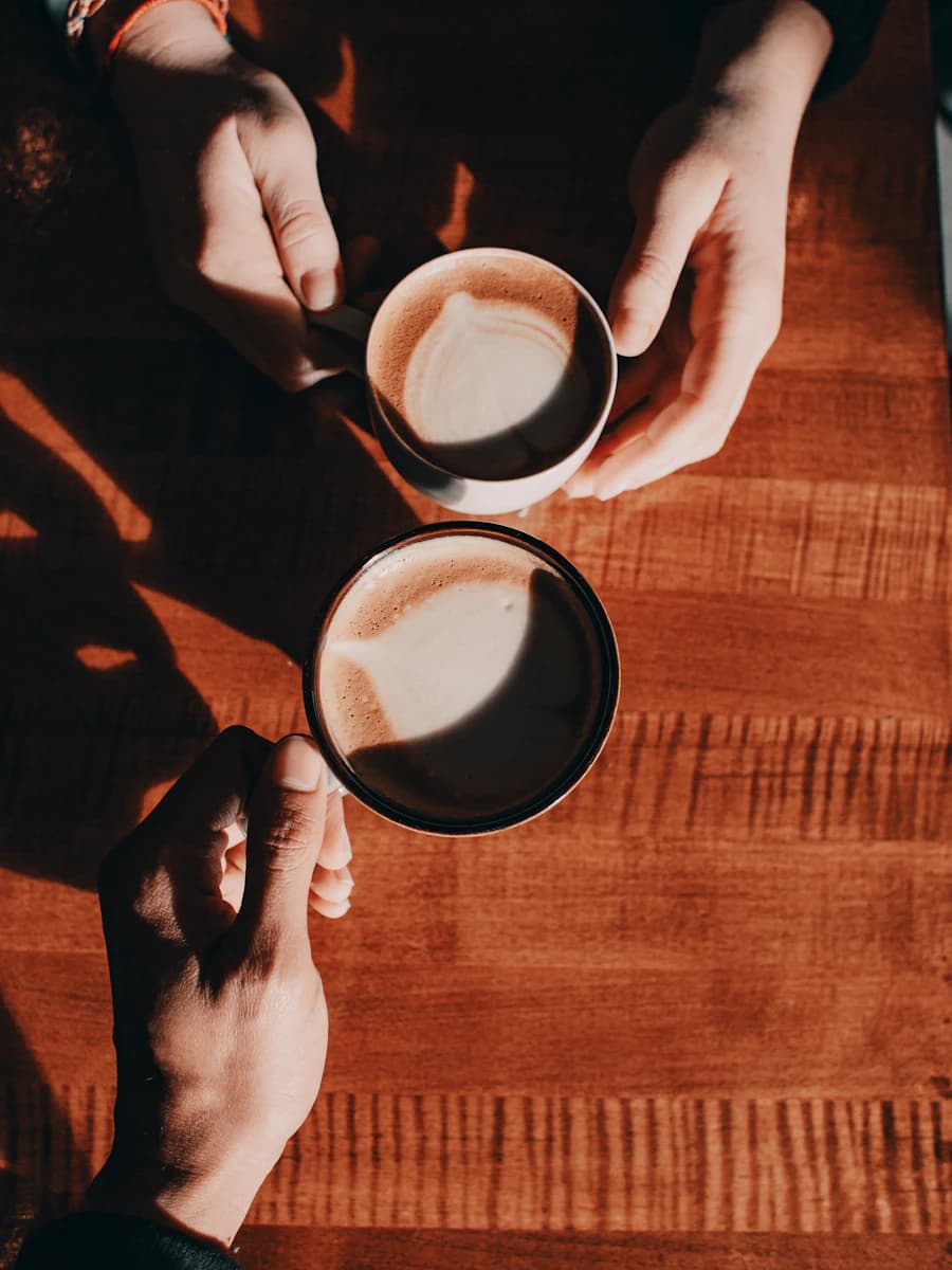 Deux tasses de café vues du dessus, tenues par deux mains sur une table en bois