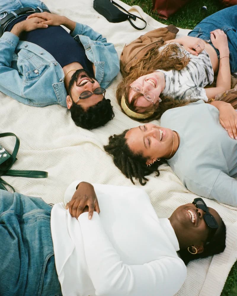 Des amis allongés sur une couverture dans l'herbe, qui rient